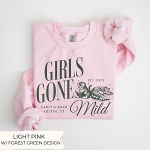 May include: Light pink sweatshirt with a forest green design. The design features the text "Girls Gone Mild" with the text "Carly's Bach Austin, TX" and "EST. 2025" below. The design also includes two cats, one reading a book and the other sleeping.