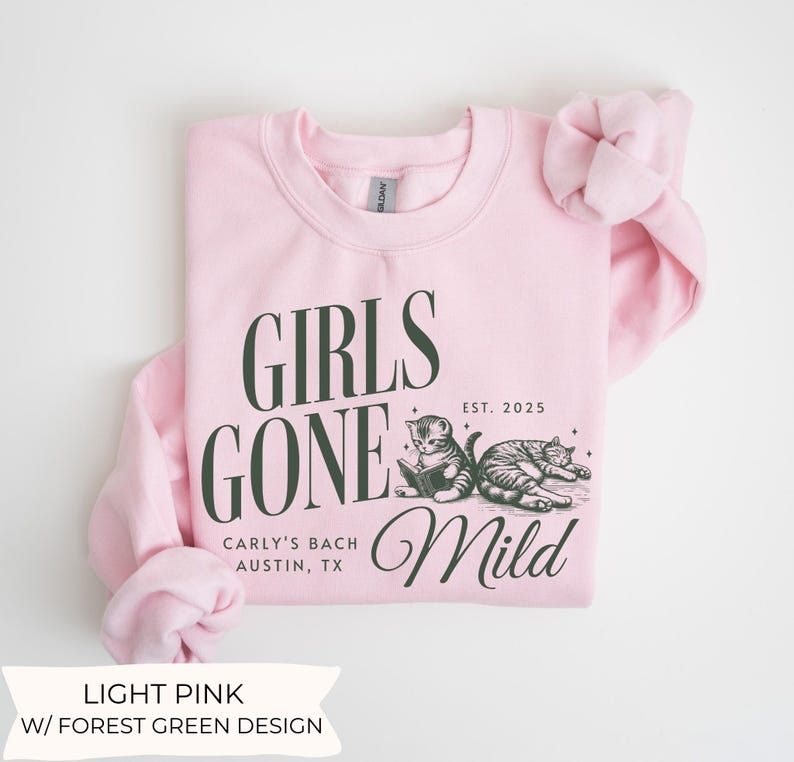 May include: Light pink sweatshirt with a forest green design. The design features the text "Girls Gone Mild" with the text "Carly's Bach Austin, TX" and "EST. 2025" below. The design also includes two cats, one reading a book and the other sleeping.