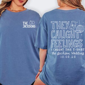 May include: A blue long-sleeve t-shirt with white text on the front and back. The front says "THE JACKSONS" with wedding rings. The back says "THEY CAUGHT FEELINGS" with a ring box and disco ball. The date "10.05.25" is also printed.