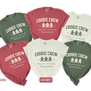 May include: Five t-shirts in different colors with a gingerbread cookie graphic and the text "Cookie Crew Est. 24 Rollin' With My Doughmies". The colors are crimson, ivory, moss, and two shades of green.