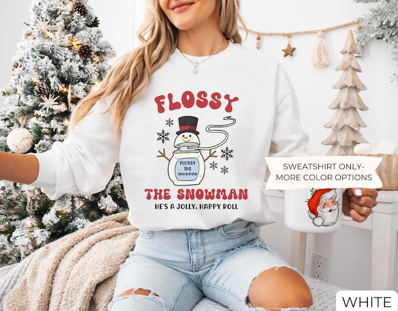 May include: White sweatshirt with the text "FLOSSY THE SNOWMAN" in red and black. The design features a snowman with a top hat and snowflakes. The phrase "HE'S A JOLLY, HAPPY ROLL" is also printed on the shirt.