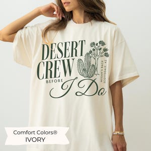 May include: A white t-shirt with the text "Desert Crew Before I Do" and a cactus graphic. The text "Megan's Bach Scottsdale, AZ" is also on the shirt. The shirt is labeled "Comfort Colors® Ivory."