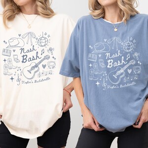 May include: Two t-shirts with a Nashville hen party theme. The shirt on the left is ivory with a white design. The shirt on the right is blue jean with a white design. Both shirts feature a guitar, a cowboy hat, a disco ball, and the text "Nash Bash Taylor's Bachelorette".