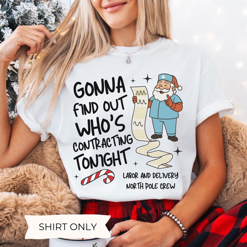 Puede incluir: Camiseta blanca con el texto "GONNA FIND OUT WHO'S CONTRACTING TONIGHT" y un dibujo animado de Pap&aacute; Noel con uniforme quir&uacute;rgico sosteniendo una lista. La camiseta tambi&eacute;n tiene un gr&aacute;fico de bast&oacute;n de caramelo y dice "LABOR AND DELIVERY NORTH POLE CREW".