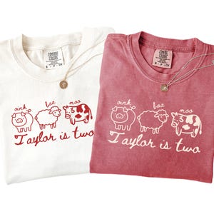 May include: Two Comfort Colors t-shirts, one white and one red, with a farm animal graphic and the text "Taylor is two." Each shirt has a gold necklace with a pendant. The graphic includes a pig, sheep, and cow.