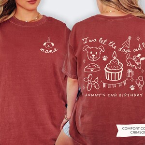 以下が含まれることがあります： 白のグラフィックが施されたクリムゾンカラーのTシャツ。前面にはパーティーハットをかぶった犬と「mama」の文字が描かれています。背面には「I wa let the dogs out?」の文字と犬をテーマにした誕生日のイラスト、「Jonny's 2nd Birthday」が描かれています。