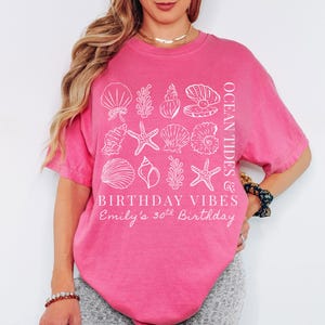 May include: A bright pink t-shirt with white seashell graphics and the text "OCEAN TIDES" and "BIRTHDAY VIBES". The shirt also includes the text "Emily's 30th Birthday".