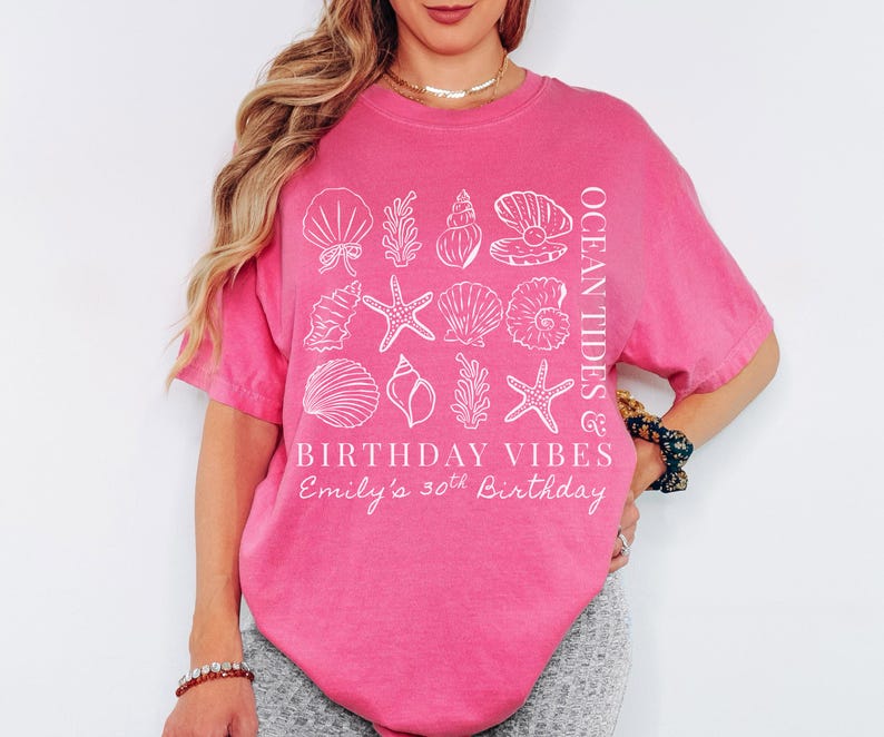May include: A bright pink t-shirt with white seashell graphics and the text "OCEAN TIDES" and "BIRTHDAY VIBES". The shirt also includes the text "Emily's 30th Birthday".