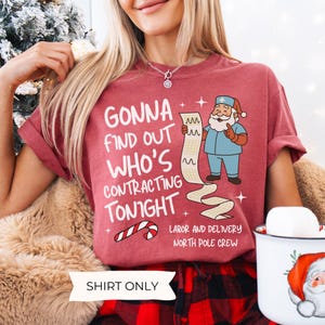 Puede incluir: Una camiseta granate con el texto "GONNA FIND OUT WHO'S CONTRACTING TONIGHT" y una caricatura de Pap&aacute; Noel con uniforme quir&uacute;rgico sosteniendo una tabla m&eacute;dica. La camiseta tambi&eacute;n dice "LABOR AND DELIVERY NORTH POLE CREW" y "SHIRT ONLY".
