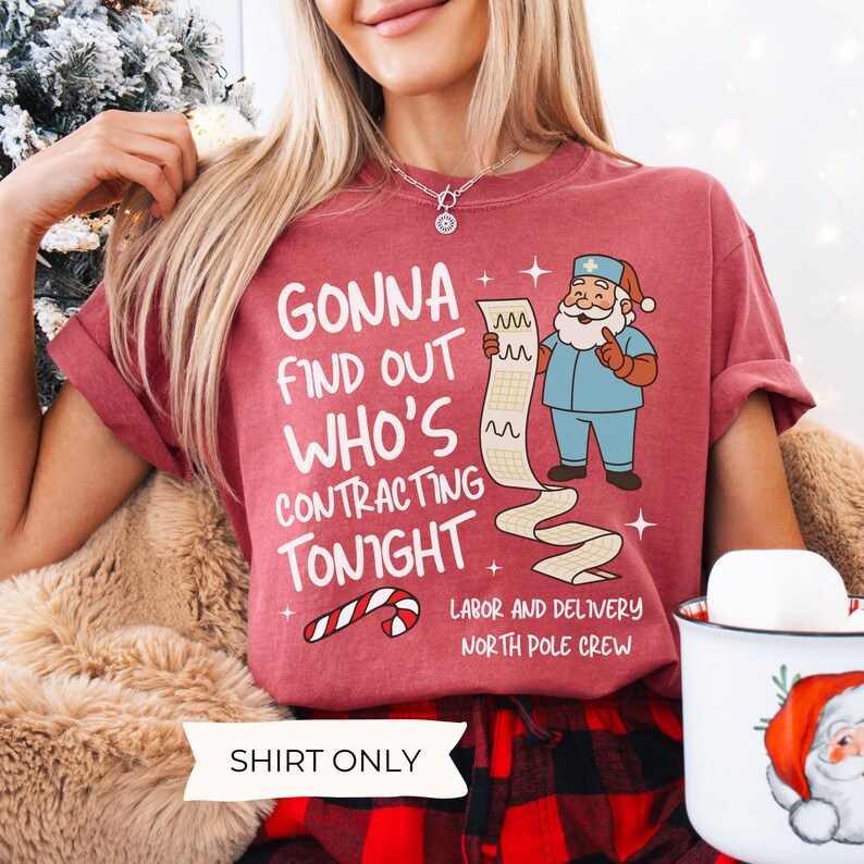 Puede incluir: Una camiseta granate con el texto "GONNA FIND OUT WHO'S CONTRACTING TONIGHT" y una caricatura de Pap&aacute; Noel con uniforme quir&uacute;rgico sosteniendo una tabla m&eacute;dica. La camiseta tambi&eacute;n dice "LABOR AND DELIVERY NORTH POLE CREW" y "SHIRT ONLY".