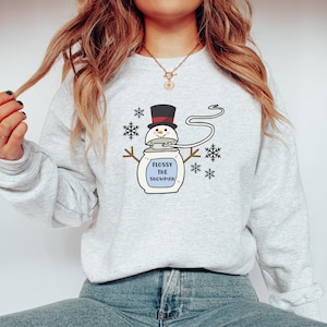 May include: A grey sweatshirt with a white graphic of a snowman with a floss container on his head. The text "Flossy the Snowman" is written on the container. The graphic is surrounded by snowflakes.
