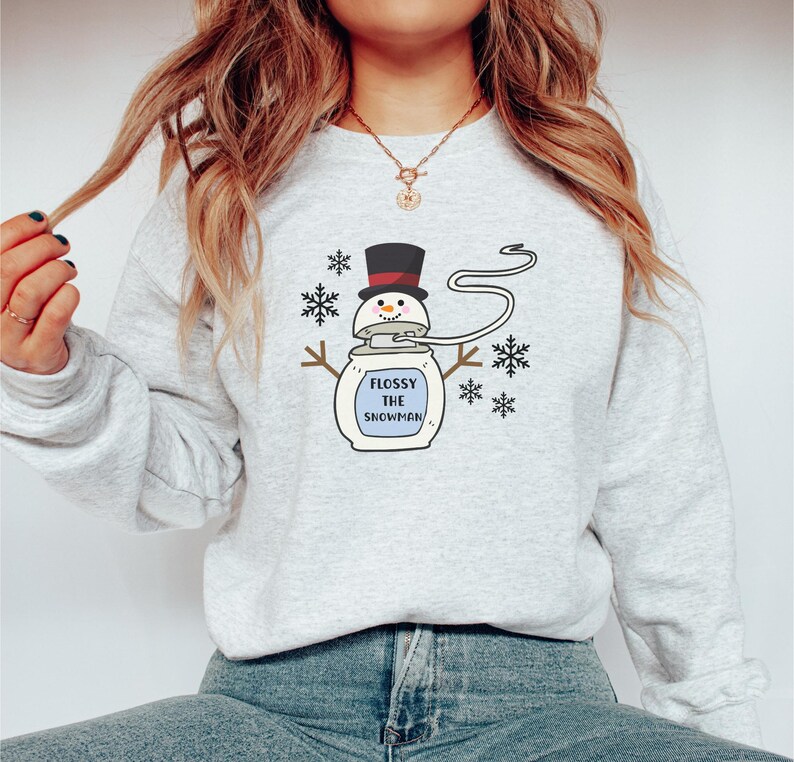 May include: A grey sweatshirt with a white graphic of a snowman with a floss container on his head. The text "Flossy the Snowman" is written on the container. The graphic is surrounded by snowflakes.