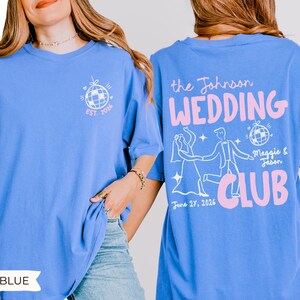 May include: Flo blue t-shirt with a white and pink graphic. The front features a disco ball design and "EST. 2026". The back displays "the Johnson WEDDING CLUB" with a dancing couple, disco ball, and the date "June 27, 2026".
