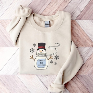 May include: A beige sweatshirt featuring a cartoon snowman wearing a black top hat and holding a sign that reads "Flossy the Snowman".