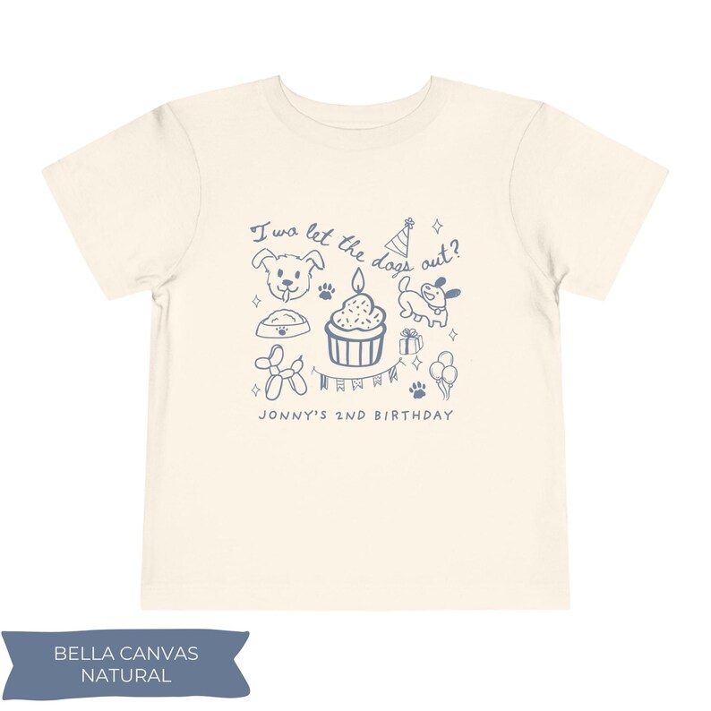 以下が含まれることがあります： クリーム色の子供用Tシャツ。青色のグラフィックには犬のイラスト、ろうそく付きのカップケーキ、そして「I wo let the dogs out?」と「JONNY'S 2ND BIRTHDAY」の文字が含まれています。