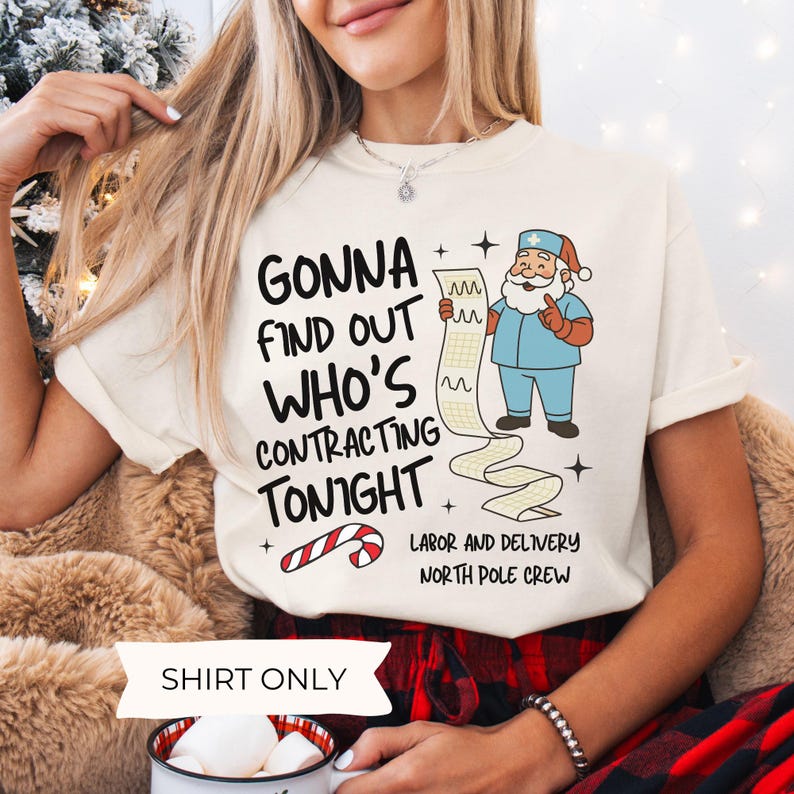 Puede incluir: Camiseta color crema con el texto "GONNA FIND OUT WHO'S CONTRACTING TONIGHT". Un Pap&aacute; Noel de dibujos animados con uniforme azul sostiene una larga lista. Tambi&eacute;n hay un gr&aacute;fico de bast&oacute;n de caramelo. La camiseta es parte de la colecci&oacute;n "Labor and Delivery North Pole Crew".