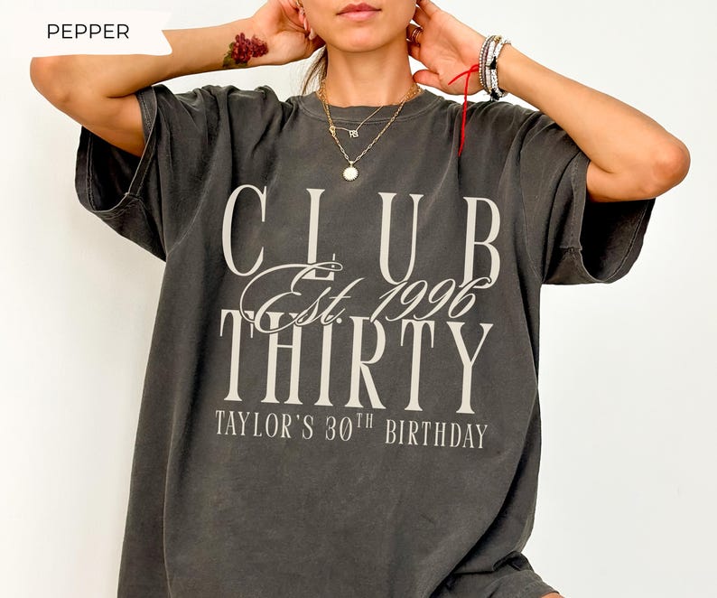 May include: A charcoal gray short-sleeve t-shirt featuring the white text CLUB Est. 1996 THIRTY and TAYLOR'S 30TH BIRTHDAY printed on the front. The shirt has a crew neckline and a relaxed fit, with the word PEPPER displayed in the top left corner.