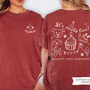 May include: Crimson-colored t-shirt with white graphic text and illustrations. The front features the word "mama" with a dog wearing a party hat. The back says "It's pawty time!" with dog-themed birthday graphics and "Jonny's First Birthday".