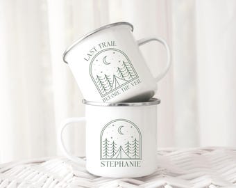 Könnte beinhalten: Zwei weiße Emailletassen mit Camping-Motiv. Die obere Tasse trägt den Text "Last Trail Before The Veil" und eine grüne Silhouette eines Waldes mit einer Mondsichel und Sternen. Die untere Tasse trägt den Text "Stephanie" und eine grüne Silhouette eines Waldes mit einer Mondsichel und Sternen.