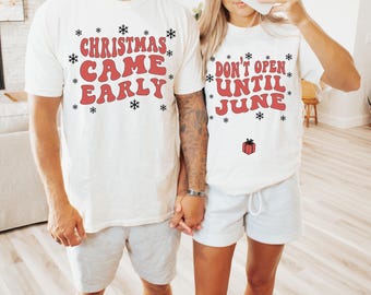 May include: A couple wearing white t-shirts with red text. The man's shirt says "Christmas Came Early" and the woman's shirt says "Don't Open Until June".
