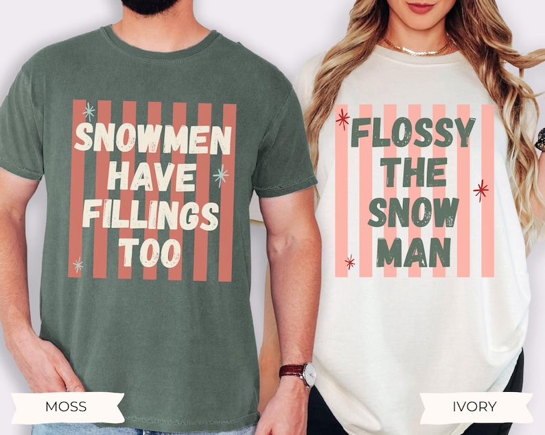 K&ouml;nnte beinhalten: Ein moosgr&uuml;nes T-Shirt mit dem Text SNOWMEN HAVE FILLINGS TOO und ein elfenbeinfarbenes T-Shirt mit dem Text FLOSSY THE SNOW MAN. Beide T-Shirts zeigen einen Hintergrund aus vertikalen korallenfarbenen Streifen und kleinen Sternen im Used-Look.