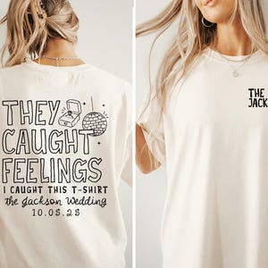 May include: Cream-colored t-shirt with black text and graphics. The back of the shirt says "THEY CAUGHT FEELINGS" with a ring box and disco ball graphic. The front has "THE JACKSONS" and rings.