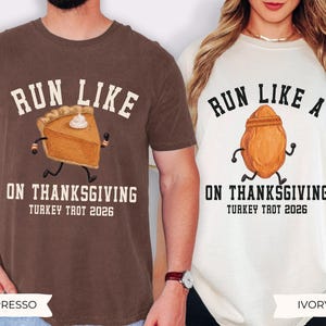 May include: A brown t-shirt with a graphic of a running pumpkin pie slice and the text RUN LIKE PIE ON THANKSGIVING TURKEY TROT 2026, and an ivory t-shirt with a running roasted turkey graphic and the text RUN LIKE A TURKEY ON THANKSGIVING TURKEY TROT 2026.