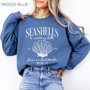 May include: Indigo blue sweatshirt with the text "Seashells & wedding bells" and a seashell graphic. The text "Est. 2025" and "Jessica's Bachelorette Miami, FL" is also printed on the sweatshirt.