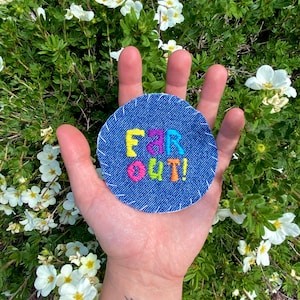 May include: A round denim patch with the words "FAR OUT!" embroidered in colorful thread.