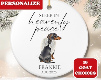 May include: A white ceramic Christmas ornament with a dachshund wearing angel wings. The ornament reads "Sleep in Heavenly Peace" and "Frankie, Aug 2025". The word "Personalize" is in a red box. A red box says "16 Coat Choices".