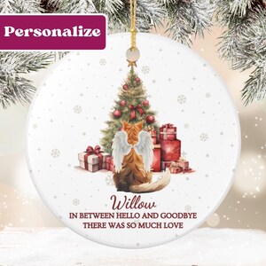 May include: A white ceramic Christmas ornament featuring a ginger cat with angel wings, a decorated Christmas tree, and wrapped gifts. The ornament has the name "Willow" and the text "In between hello and goodbye there was so much love."
