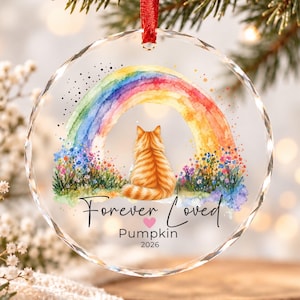 May include: A round, faceted glass ornament featuring a watercolour illustration of an orange tabby cat sitting before a colourful rainbow and wildflowers. The text reads Forever Loved, Pumpkin, and 2026, with a small pink heart between the words.