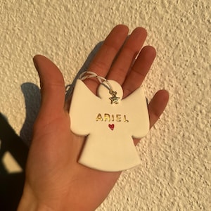 Peut inclure: Ornement d'ange en céramique blanche avec le nom "ARIEL" écrit en lettres dorées et un petit cœur rouge.