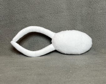 May include: A white plush toy shaped like a sperm cell, with a rounded head and two curved, elongated appendages. The toy is made of a soft, textured fabric and is set against a gray background.