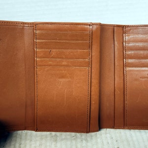 May include: A brown leather trifold wallet with multiple card slots and a snap closure. The wallet has the text "Tuscany Leather" embossed on the front.