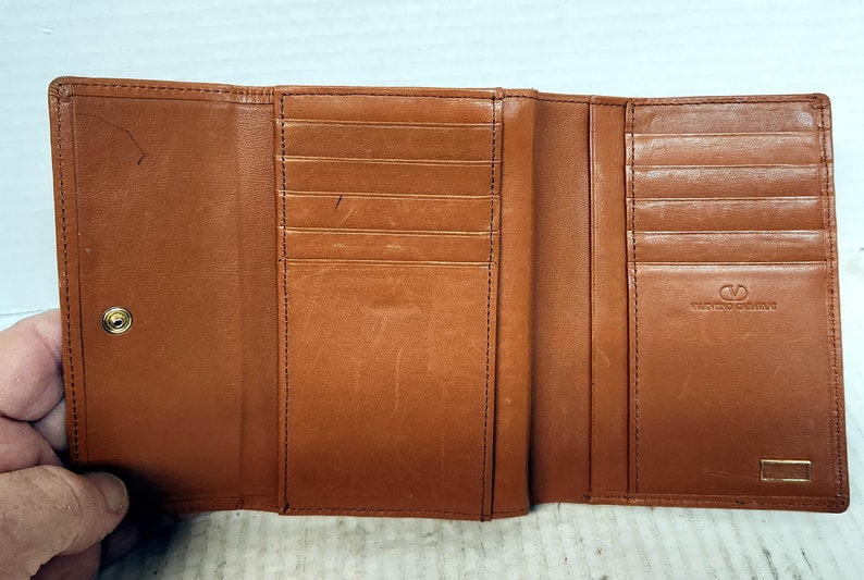 May include: A brown leather trifold wallet with multiple card slots and a snap closure. The wallet has the text "Tuscany Leather" embossed on the front.