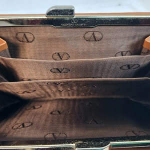 May include: A brown leather wallet with a gold clasp and multiple card slots. The interior is lined with brown fabric and features the Valentino Garavani logo.