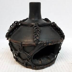 May include: Black ceramic ashtray with a woven leather and wood design. The ashtray has a round opening in the centre.