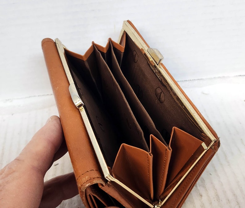 May include: A brown leather wallet with a gold metal clasp. The wallet has multiple compartments and is folded closed.