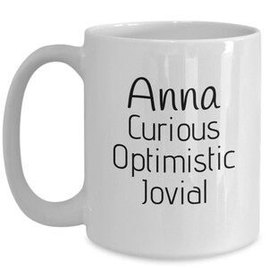Puede incluir: Taza de caf&eacute; de cer&aacute;mica blanca con una inscripci&oacute;n negra que dice "Anna curiosa optimista jovial".