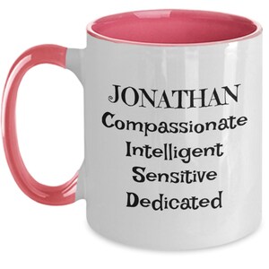 May include: White ceramic coffee mug with a pink rim and handle. The mug has black text that reads "JONATHAN Compassionate Intelligent Sensitive Dedicated".