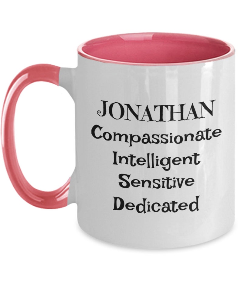 May include: White ceramic coffee mug with a pink rim and handle. The mug has black text that reads "JONATHAN Compassionate Intelligent Sensitive Dedicated".