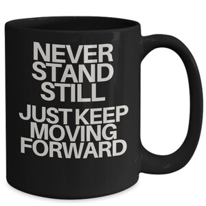 May include: Black coffee mug with white text that reads "Never stand still, just keep moving forward".