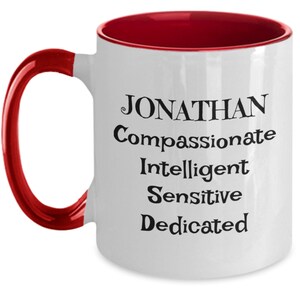 May include: White ceramic coffee mug with a red rim and handle. The mug has black text that reads "JONATHAN Compassionate Intelligent Sensitive Dedicated".
