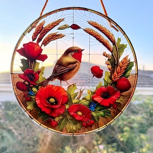 May include: Circular stained glass window art depicting a bird with a red breast amidst red poppies, green leaves, and wheat. The design is framed within a round border and includes a hanging cord.
