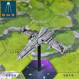 May include: A silver-colored miniature spaceship model, mounted on a black stand, is positioned above a hexagonal game board. The board features a green landscape design with numbered sections and the text "LEVEL 1". The model has detailed wings and a cockpit.