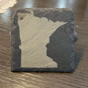 May include: A black slate coaster with a white outline of the state of Minnesota.