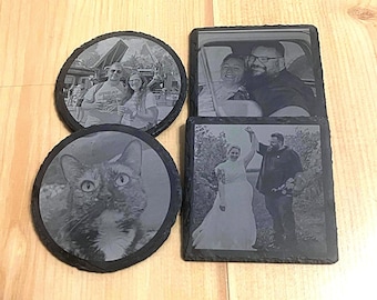 May include: Set of four black slate coasters with different images printed on them. One coaster features a couple, another features a cat, and the other two feature couples.