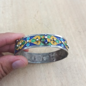 Puede incluir: Un brazalete de plata con un diseño de esmalte azul, verde y amarillo. El diseño de esmalte presenta motivos florales estilizados.