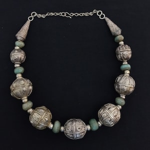 May include: A silver necklace with turquoise beads and ornate silver balls. The necklace has a silver chain with a clasp.